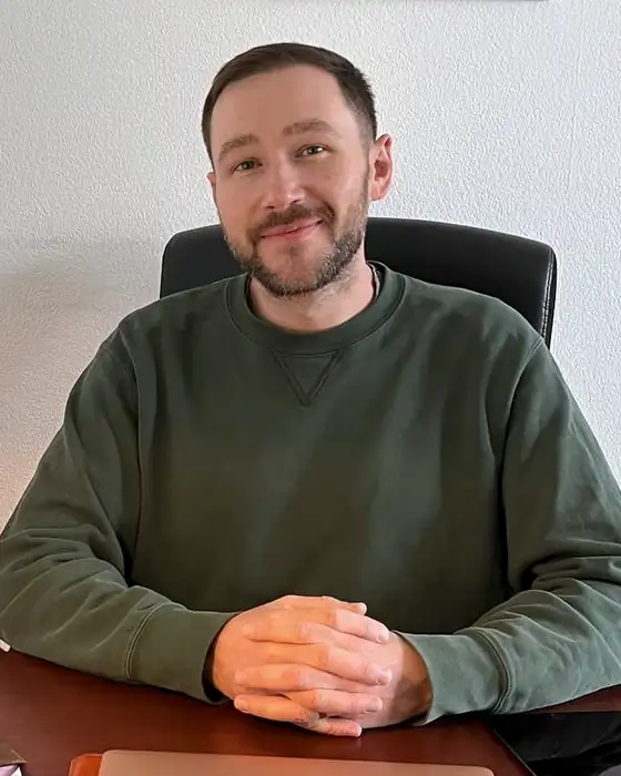 Dimitri Baitinger sitzt mit gefalteten Händen an seinem Schreibtisch